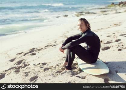 A young man sitting on his surfboard on the sand