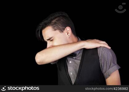 A young man sneezing into his elbow. Black background.