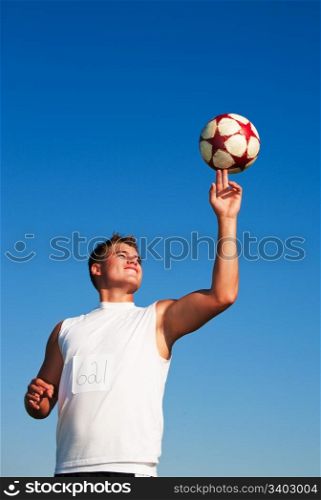 A young man spinning a soccer ball on his finger in the warm summer sun.