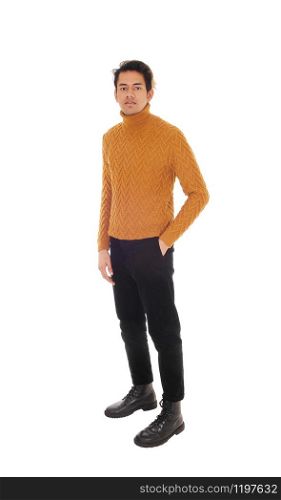 A young man standing in the studio in black jeans and gold colored sweater with one hand in his pocket, isolated for white background
