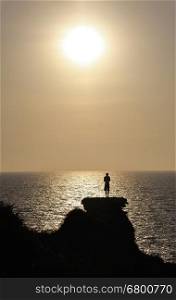 A young man stands on the remains of the Crusader wall above the sea at sunset. Mediterranean Coast Israel
