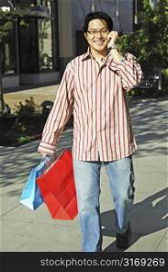 A young man talking on the phone while shopping at an outdoor shopping mall