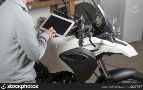 a young man using a tablet next to motorcycle