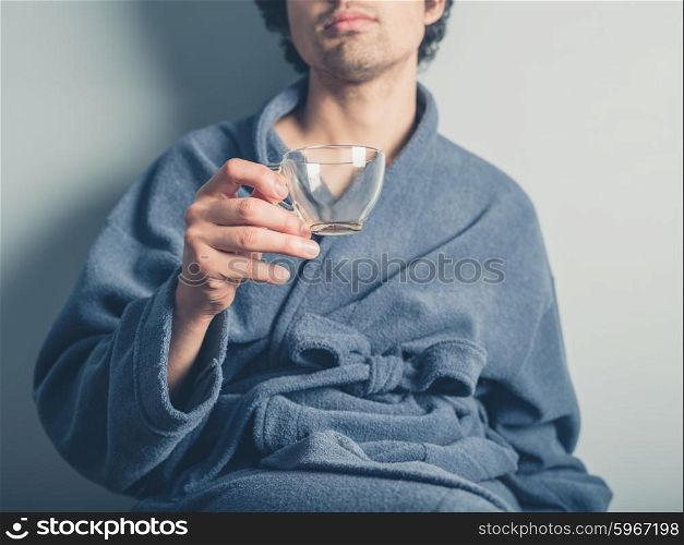 A young man wearing a bathrobe is holding an empty coffee cup