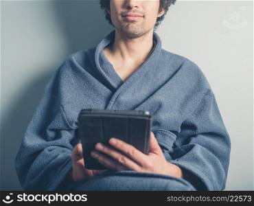 A young man wearing a bathrobe is using a tablet computer