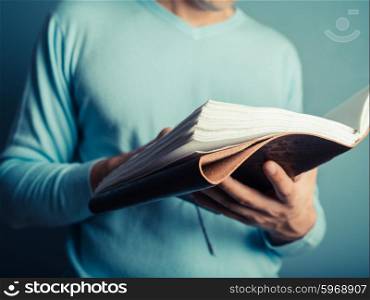 A young man wearing a blue jumper is flipping through a big notebook