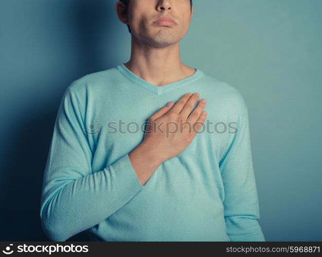 A young man wearing a blue jumper is placing his hand on his chest