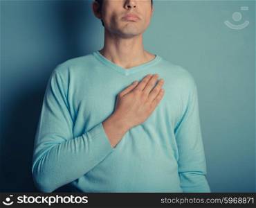 A young man wearing a blue jumper is placing his hand on his chest