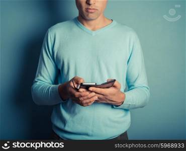 A young man wearing a blue jumper is using a smart phone