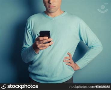 A young man wearing a blue jumper is using a smart phone