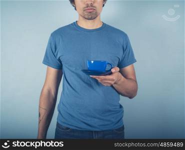 A young man wearing a blue t-shirt is holding a cup of cappucino