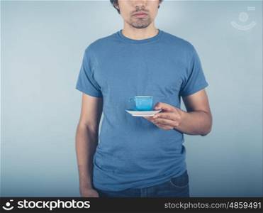 A young man wearing a blue t-shirt is holding a cup of espresso
