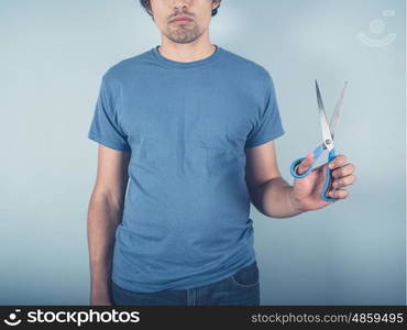 A young man wearing a blue t-shirt is holding a pair of scissors