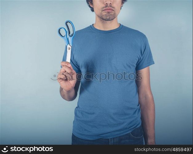 A young man wearing a blue t-shirt is holding a pair of scissors