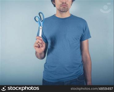 A young man wearing a blue t-shirt is holding a pair of scissors