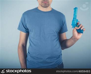 A young man wearing a blue t-shirt is holding a water pistol