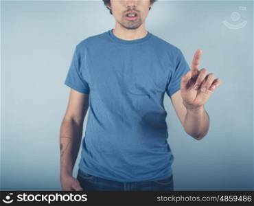 A young man wearing a blue t-shirt is raising his finger to either point or swipe or push