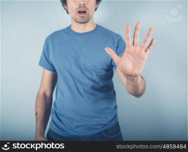 A young man wearing a blue t-shirt is raising his open hand to signal stop