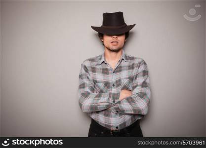 A young man wearing a cowboy hat and a plaid shirt is posing against a green wall