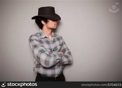 A young man wearing a cowboy hat and a plaid shirt is posing against a green wall