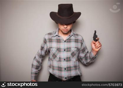 A young man wearing a cowboy hat and a plaid shirt is holding a revolver