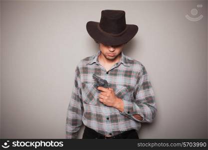 A young man wearing a cowboy hat and a plaid shirt is holding a revolver