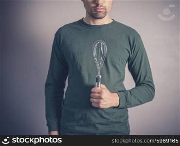 A young man wearing a green top is holding a balloon whisk