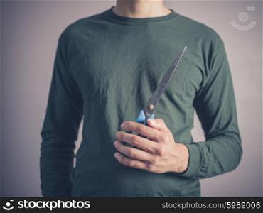 A young man wearing a green top is holding a pair of scissors