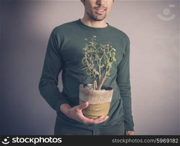 A young man wearing a green top is holding a potted plant