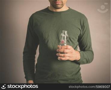 A young man wearing a green top is holding a small glass bottle