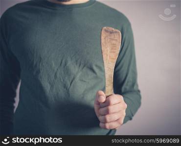 A young man wearing a green top is holding a wooden spatula
