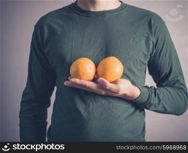 A young man wearing a green top is holding two oranges