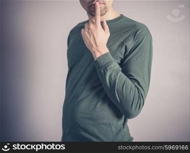 A young man wearing a green top is looking concerned and thoughtful with his finger on his lips