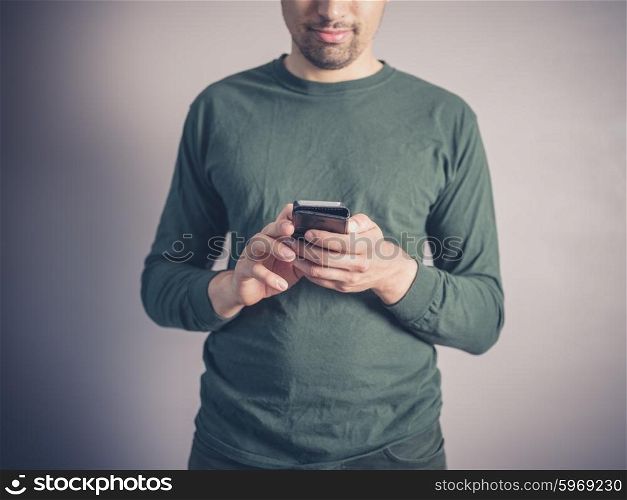 A young man wearing a green top is using a smart phone