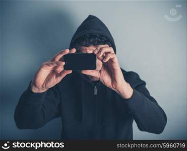 A young man wearing a hooded top is taking photos with his smartphone
