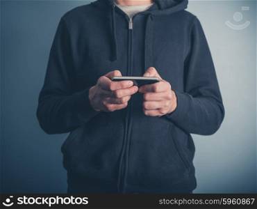 A young man wearing a hooded top is using his smartphone