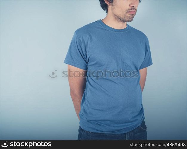 A young man wearing a t-shirt is standing by a blue wall