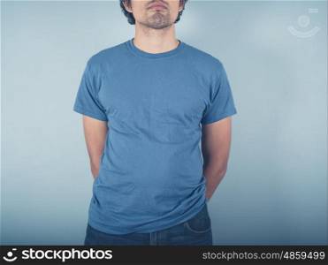 A young man wearing a t-shirt is standing by a blue wall