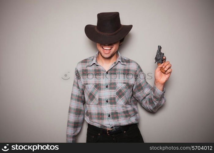 A young man wearing acowboy hat and a plaid shirt is holding a revolver