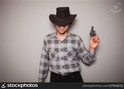 A young man wearing acowboy hat and a plaid shirt is holding a revolver