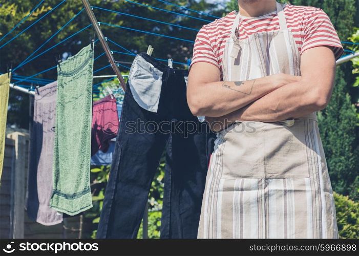 A young man wearing an apron is standing by a clothes line in the garden