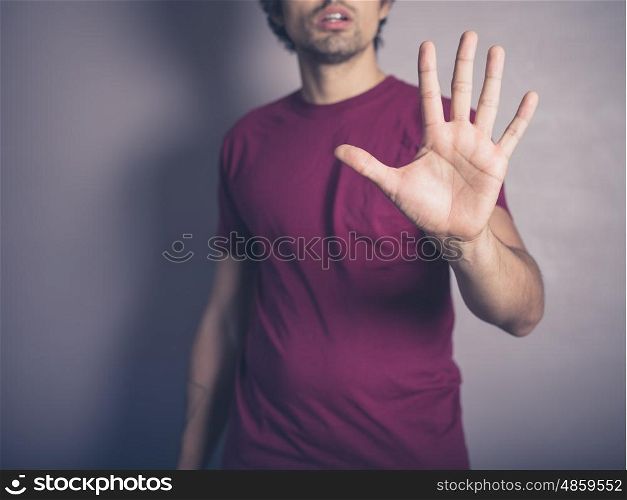 A young man wearing purple is raising his open hand to signal stop