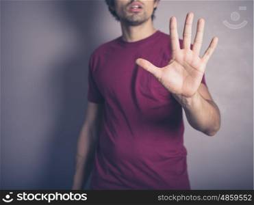 A young man wearing purple is raising his open hand to signal stop