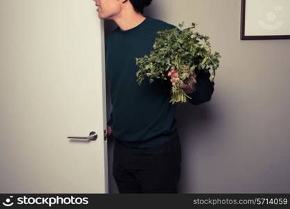 A young man with a big bunch of parsley in his hand is answering the door