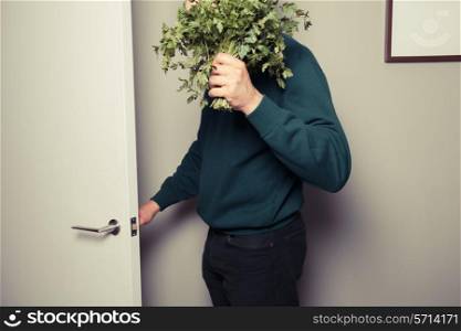 A young man with a big bunch of parsley in his hand is answering the door