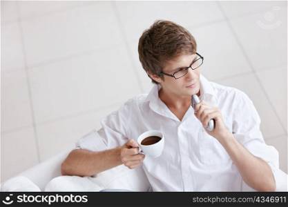 A young man with a cup of coffee and a remote control in hand
