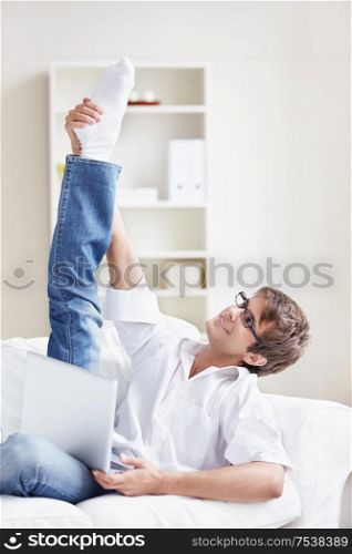 A young man with a raised foot with the laptop at home