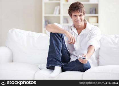 A young man with a remote control in the hands of TV changes channels