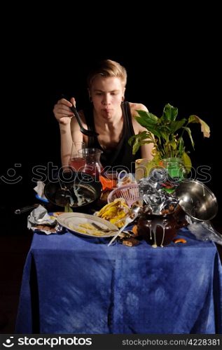 A young man with a spoon sits behind dirty table