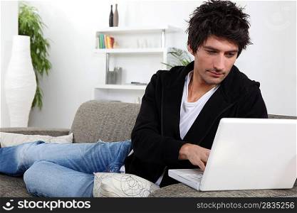 A young man with his laptop on the sofa.